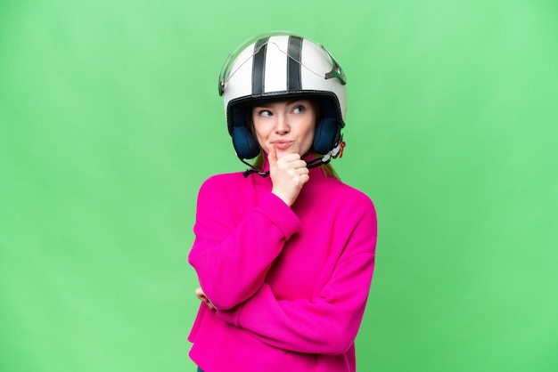 Mujer bonita joven con un casco de motocicleta sobre un fondo clave de croma aislado que tiene dudas y pensamiento