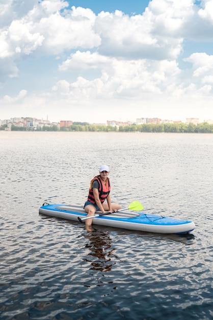 Mujer bonita joven en chalecos salvavidas naranjas surfea en supboard en el lago de la ciudad