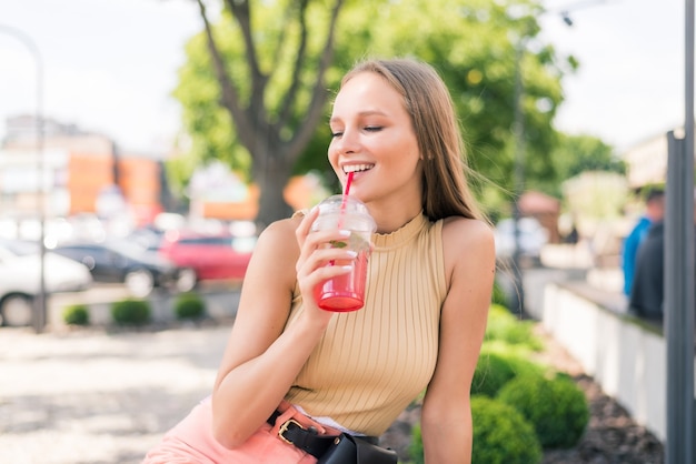 Mujer bonita joven con cóctel en la cafetería de la calle