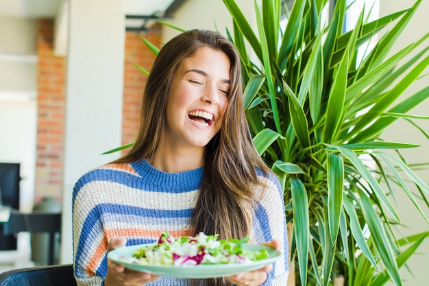 Mujer bonita joven comiendo una ensalada en casa