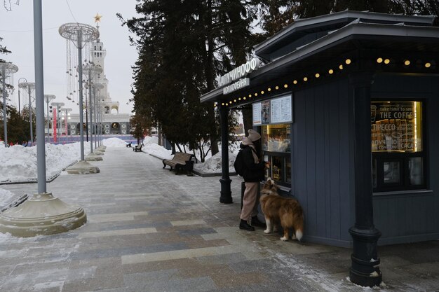 Mujer bonita joven compra café en la tienda de comida rápida en el parque en invierno perro de pie junto a