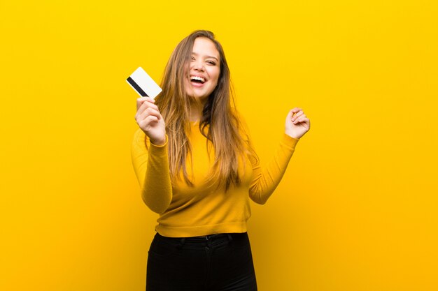 Mujer bonita joven dinero o concepto de compras contra la pared amarilla