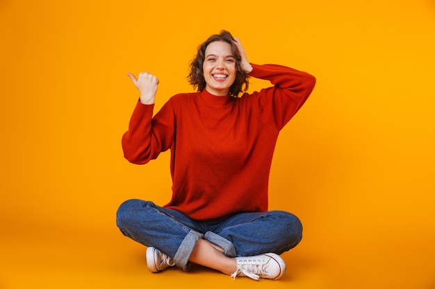 mujer bonita joven emocional que presenta aislada en la pared amarilla que muestra el copyspace.