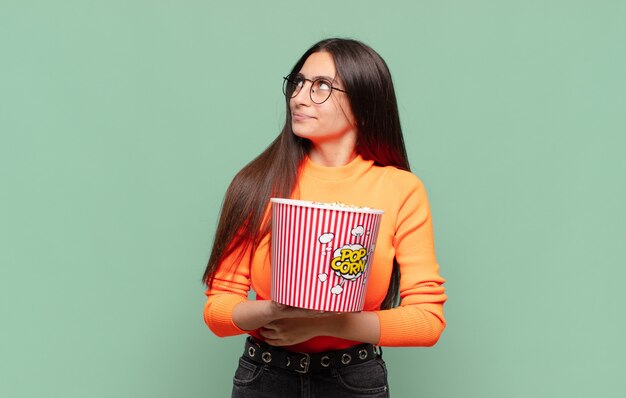 Mujer bonita joven encogiéndose de hombros, sintiéndose confusa e insegura, dudando con los brazos cruzados y la mirada perpleja. concepto de palomitas de maíz