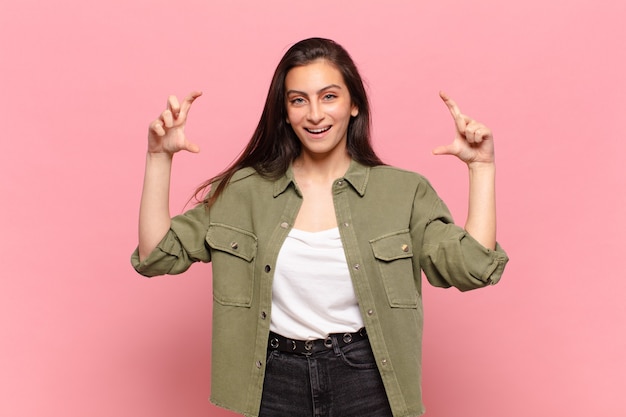 Mujer bonita joven enmarcando o delineando su propia sonrisa con ambas manos, mirando positivo y feliz, concepto de bienestar