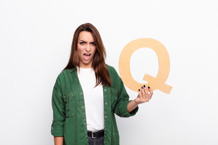 Foto mujer bonita joven enojada, enojada, en desacuerdo, sosteniendo la letra q del alfabeto para formar una palabra o una oración.