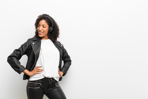 Foto mujer bonita joven escuchando música con auriculares con una chaqueta de cuero sobre pared blanca