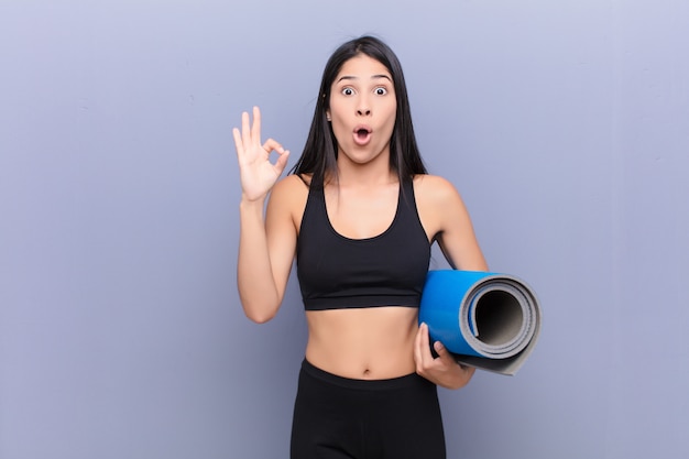 Mujer bonita joven con una estera de yoga sobre pared de cemento