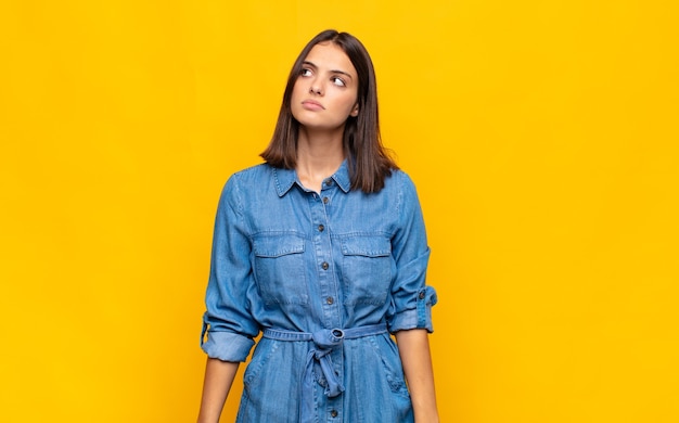 Mujer bonita joven con una expresión preocupada, confundida, despistada, mirando hacia arriba para copiar el espacio, dudando