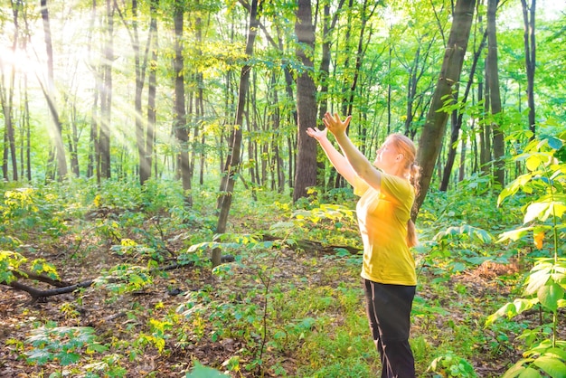 Mujer bonita joven feliz extendiendo las manos a la luz del sol en el bosque