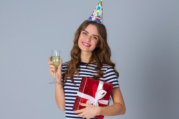 Mujer bonita joven en gorra de celebración con cabello largo sosteniendo un regalo rojo y mirándolo