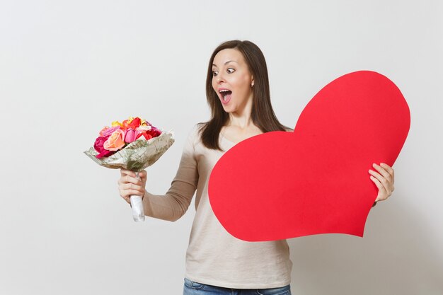 Mujer bonita joven con gran corazón rojo, ramo de flores rosas hermosas sobre fondo blanco. Copie el espacio para publicidad. Lugar para el texto. Concepto del Día de San Valentín o Día Internacional de la Mujer