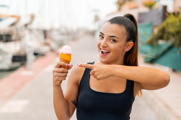 Mujer bonita joven con un helado de cucurucho al aire libre y apuntándolo