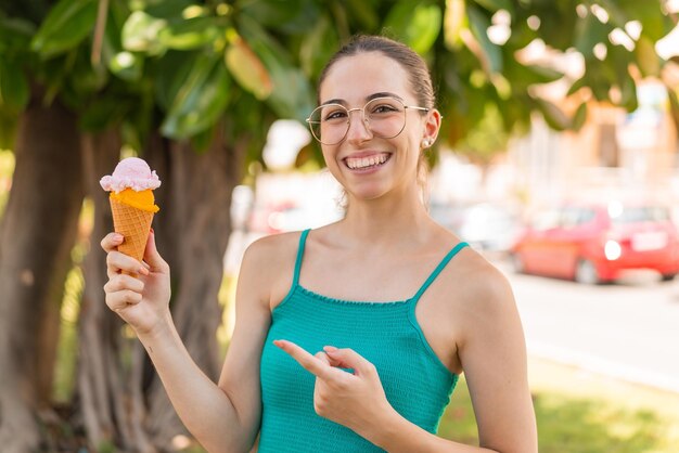 Mujer bonita joven con un helado de cucurucho al aire libre y apuntándolo