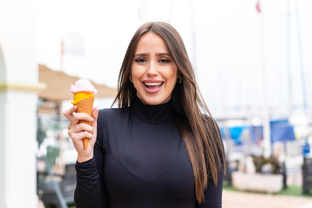 Mujer bonita joven con un helado de cucurucho al aire libre con sorpresa y expresión facial conmocionada