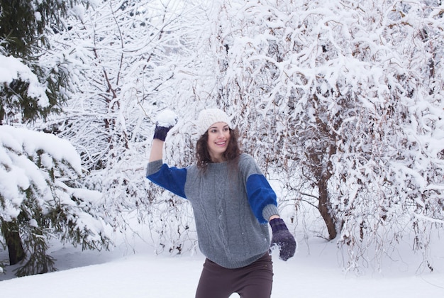 Mujer bonita joven jugando lucha de bolas de nieve en un bosque de invierno