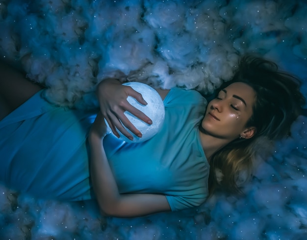 Mujer bonita joven con la luna llena y las nubes en el primer plano de fondo azul estrellado.Procesamiento de arte