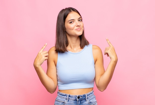 Mujer bonita joven con una mala actitud que parece orgullosa y agresiva, apuntando hacia arriba o haciendo un signo divertido con las manos