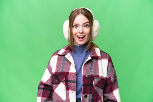 Mujer bonita joven con manguitos de invierno sobre un fondo clave de croma aislado con expresión facial sorpresa