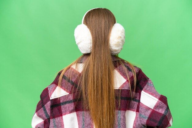 Mujer bonita joven con manguitos de invierno sobre fondo de clave de croma aislado en posición trasera