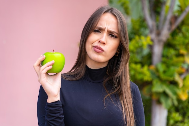 Mujer bonita joven con una manzana al aire libre con expresión triste