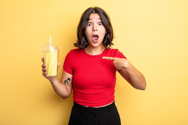 Mujer bonita joven mirando conmocionado y sorprendido con la boca abierta, apuntando a sí mismo. concepto de batido