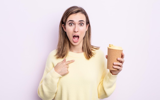 Mujer bonita joven mirando conmocionado y sorprendido con la boca abierta, apuntando a sí mismo. concepto de café para llevar