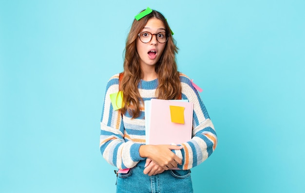 Mujer bonita joven mirando muy conmocionado o sorprendido con una bolsa y sosteniendo libros