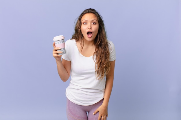 Mujer bonita joven mirando muy conmocionado o sorprendido y sosteniendo un café