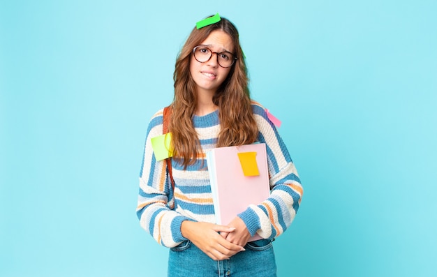 Mujer bonita joven mirando perplejo y confundido con una bolsa y sosteniendo libros