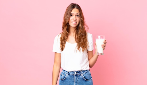 Mujer bonita joven mirando perplejo y confundido y sosteniendo un vaso de leche