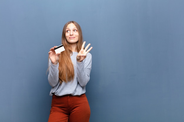 Mujer bonita joven con una pared azul de tarjeta de crédito con un copyspace