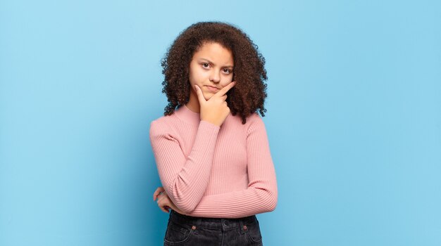 Mujer bonita joven con pelo afro y suéter rosa posando en la pared azul