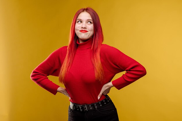Mujer bonita joven con pelo rojo y sweter rojo posando sobre fondo amarillo
