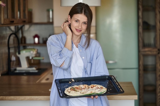 Una mujer bonita joven prepara pizza en la cocina