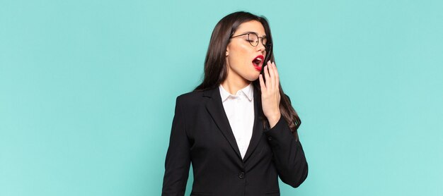 Mujer bonita joven que bosteza perezosamente temprano en la mañana, se despierta y se ve somnolienta, cansada y aburrida. concepto de negocio