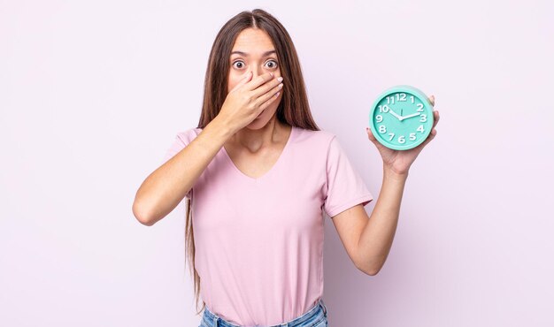 Mujer bonita joven que cubre la boca con las manos con una sorpresa. concepto de reloj despertador