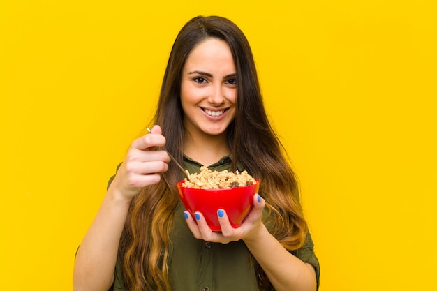 Mujer bonita joven que desayuna contra la pared anaranjada