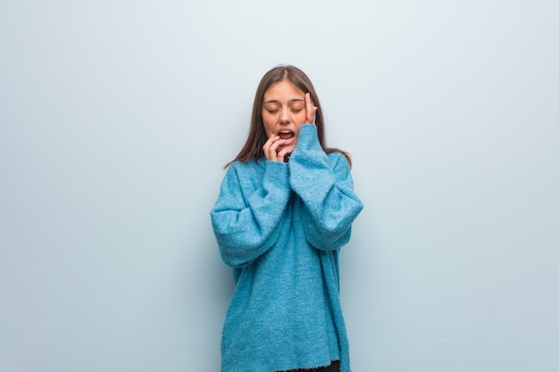 Mujer bonita joven que lleva un suéter azul desesperado y triste