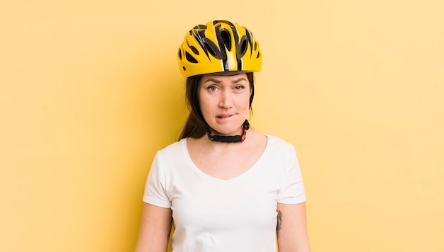 Mujer bonita joven que mira el concepto de casco de bicicleta desconcertado y confundido