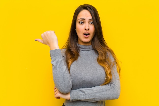 Mujer bonita joven que parece asombrada con incredulidad, apuntando al objeto a un lado y diciendo wow, trabajo increíble o concepto de negocio