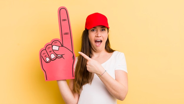 Mujer bonita joven que parece emocionada y sorprendida señalando el concepto de mano número uno del lado