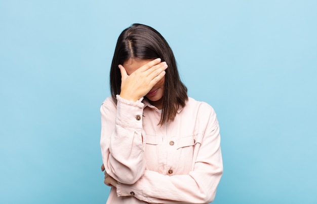 Mujer bonita joven que parece estresada, avergonzada o molesta, con dolor de cabeza, cubriendo la cara con la mano