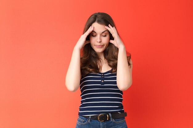 Mujer bonita joven que parece estresada y frustrada, trabajando bajo presión con dolor de cabeza y con problemas sobre la pared roja