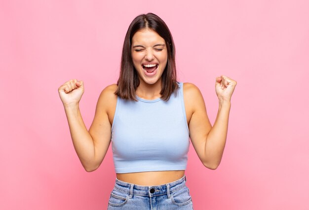 Mujer bonita joven que parece extremadamente feliz y sorprendida, celebrando el éxito, gritando y saltando