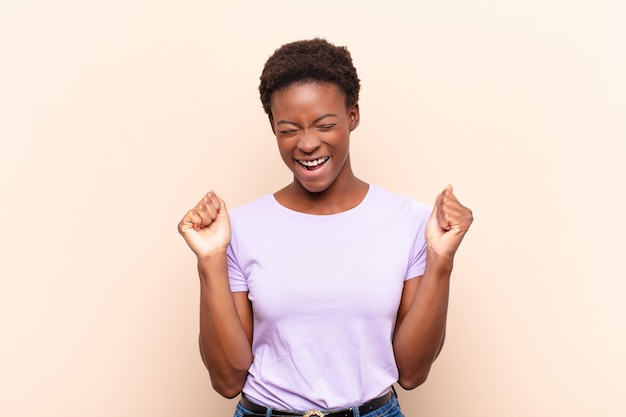 Mujer bonita joven que parece extremadamente feliz y sorprendida, celebrando el éxito, gritando y saltando