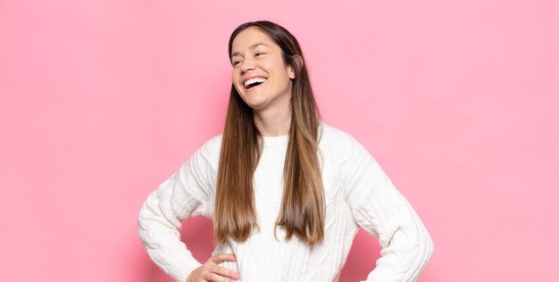 Mujer bonita joven que parece feliz, alegre y segura, sonriendo con orgullo y mirando al lado con ambas manos en las caderas