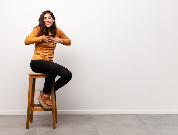 Mujer bonita joven que parece feliz y amigable, sonriendo y guiñándole un ojo con una actitud positiva sentado en una habitación