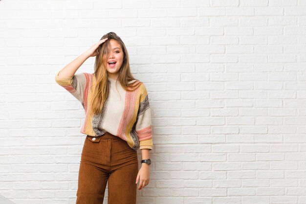 Mujer bonita joven que parece feliz, asombrada y sorprendida, sonriendo y dándose cuenta de buenas noticias increíbles e increíbles contra la pared de ladrillo