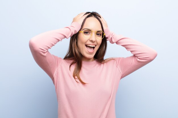 Mujer bonita joven que parece feliz, despreocupada, amigable y relajada disfrutando de la vida y el éxito, con una actitud positiva contra la pared azul